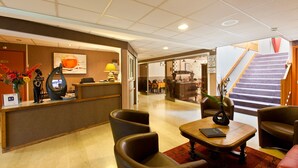 Un vestíbulo de hotel con una recepción, zona de estar y una escalera.