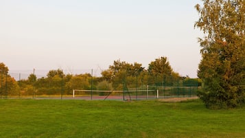 A sports field with a volleyball net, surrounded by trees and a fence.