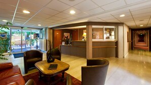 Vestíbulo de hotel con mostrador de recepción, zona de estar y vistas al exterior.