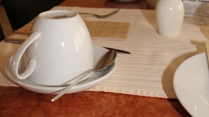 Et spisebord dækket med hvide tallerkener, en kop og en ske. En menu med teksten "Kaffeehaus" er synlig i baggrunden.