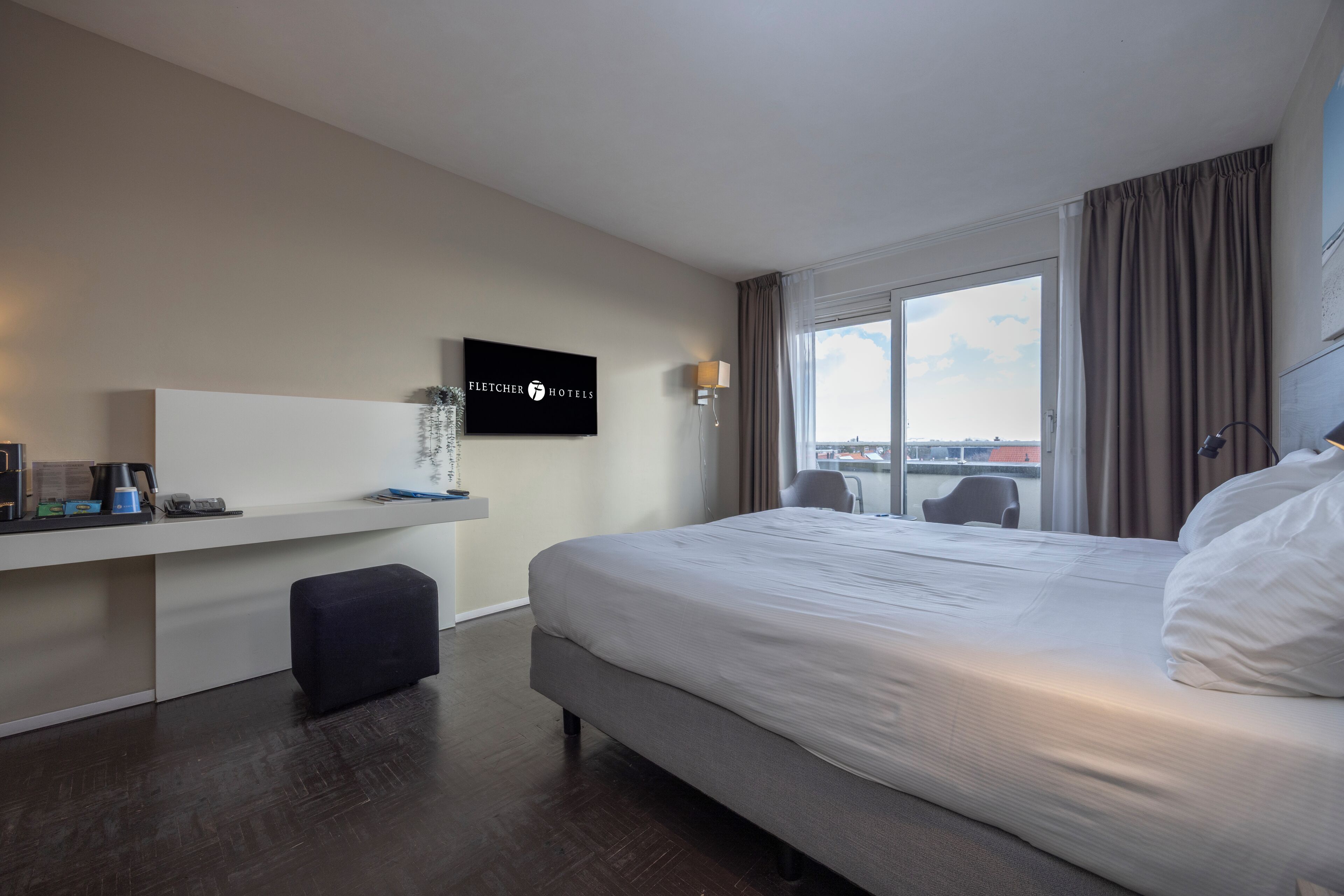 Quarto de hotel com uma cama grande, uma escrivaninha com computador, televisão e janela com vista para a cidade.
