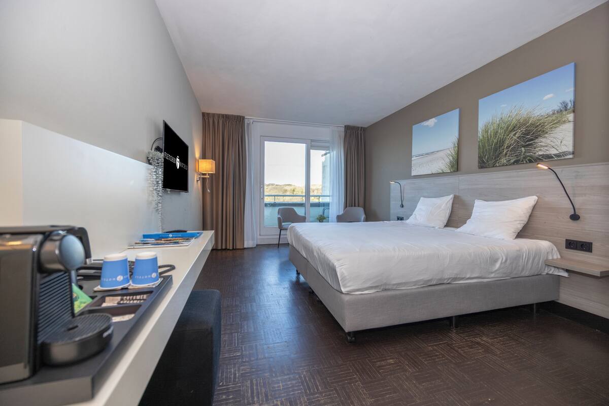 Quarto de hotel com cama, secretária com máquina de café e televisão.