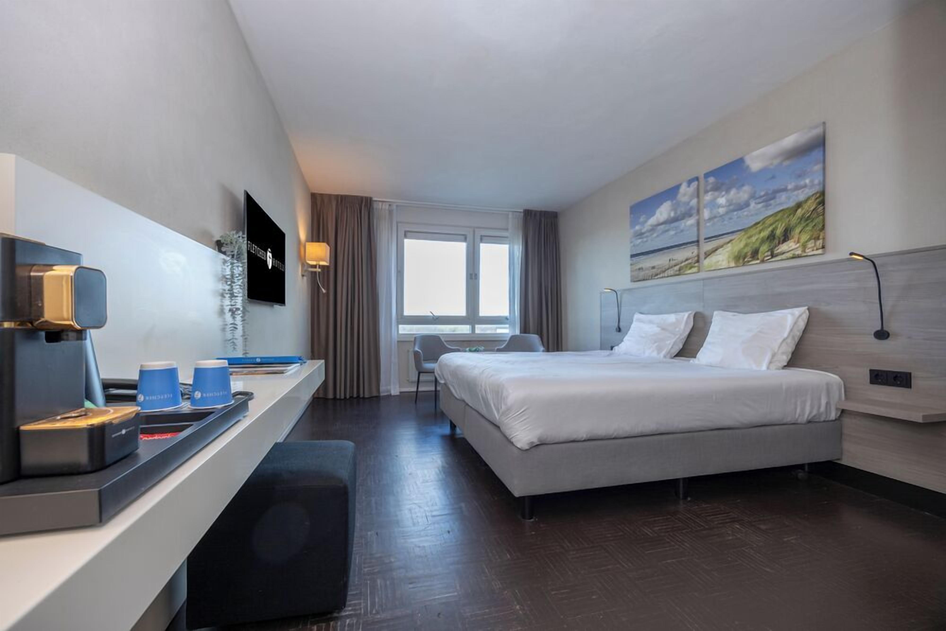 Hotelkamer met een bed, een bureau met koffieapparaat, een televisie en een raam met gordijnen.