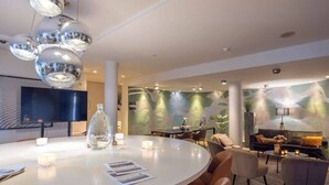 Un moderno vestíbulo de hotel con una mesa de comedor redonda, asientos cómodos, una chimenea y una gran pantalla de televisión.