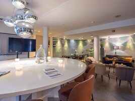 Un moderno vestíbulo de hotel con una mesa de comedor redonda, asientos cómodos, una chimenea y una gran pantalla de televisión.