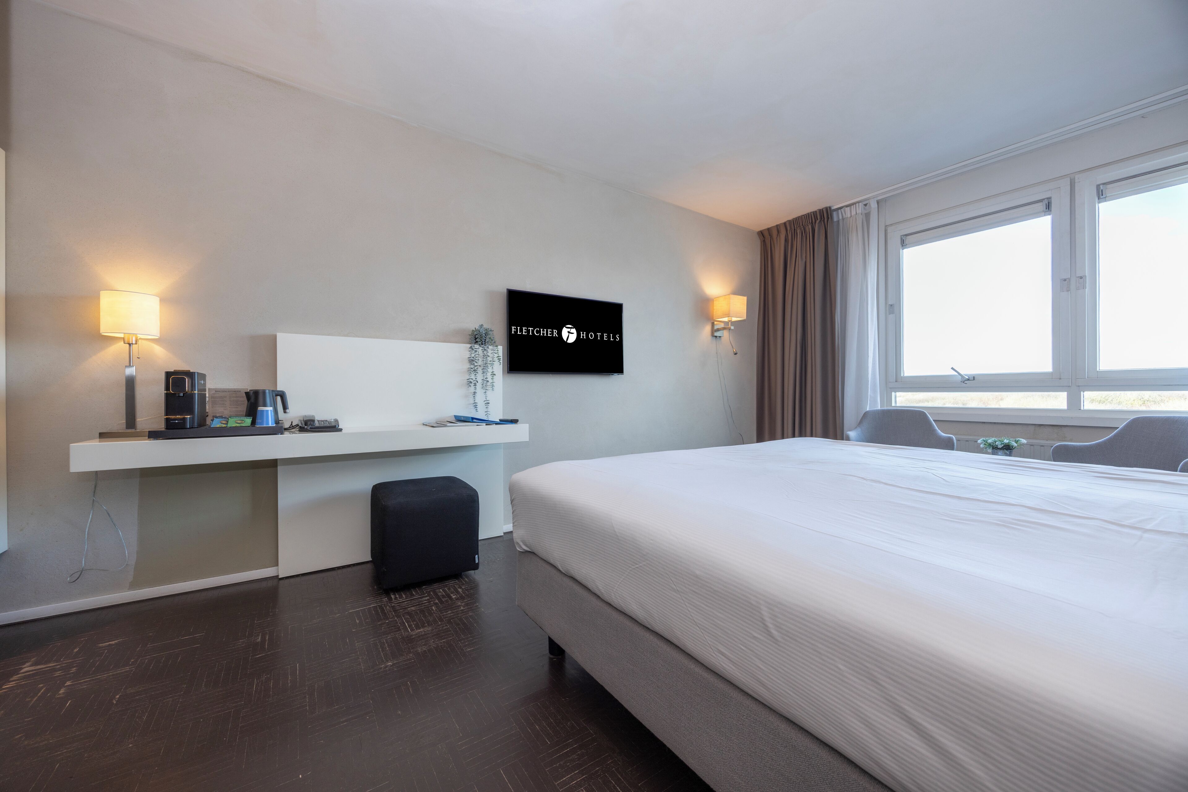 A hotel room with a large bed, a desk with a flat-screen TV, a coffee maker, and a small plant.