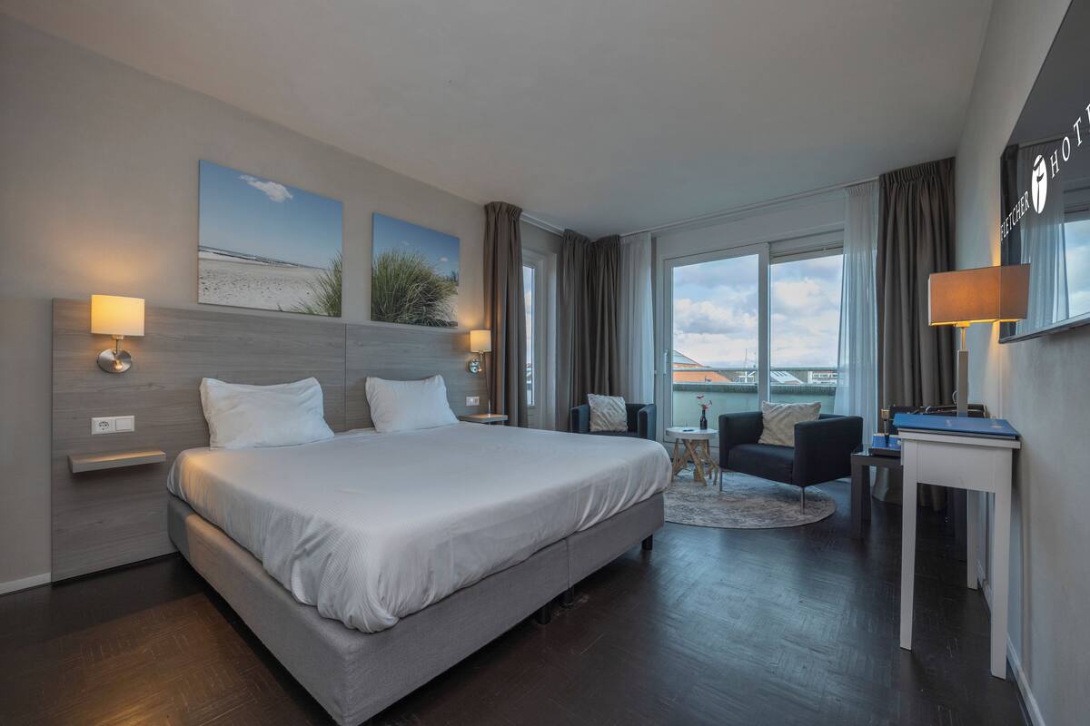 Quarto de hotel moderno com uma cama grande, uma escrivaninha e vista para a cidade.