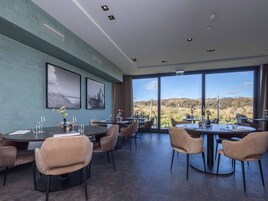 Un comedor con mesas y sillas redondas, ventanas amplias con vistas al campo y obras de arte en las paredes.