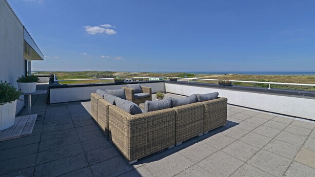 Una terraza en la azotea con un sofá de mimbre, asientos al aire libre y vistas al mar.