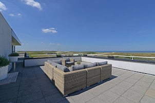 Una terraza en la azotea con un sofá de mimbre, asientos al aire libre y vistas al mar.