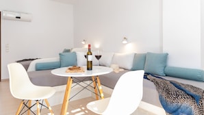 A modern living room with a white sofa, a round table with chairs, and a wine bottle. - Depis Place & Apartments (Naxos)