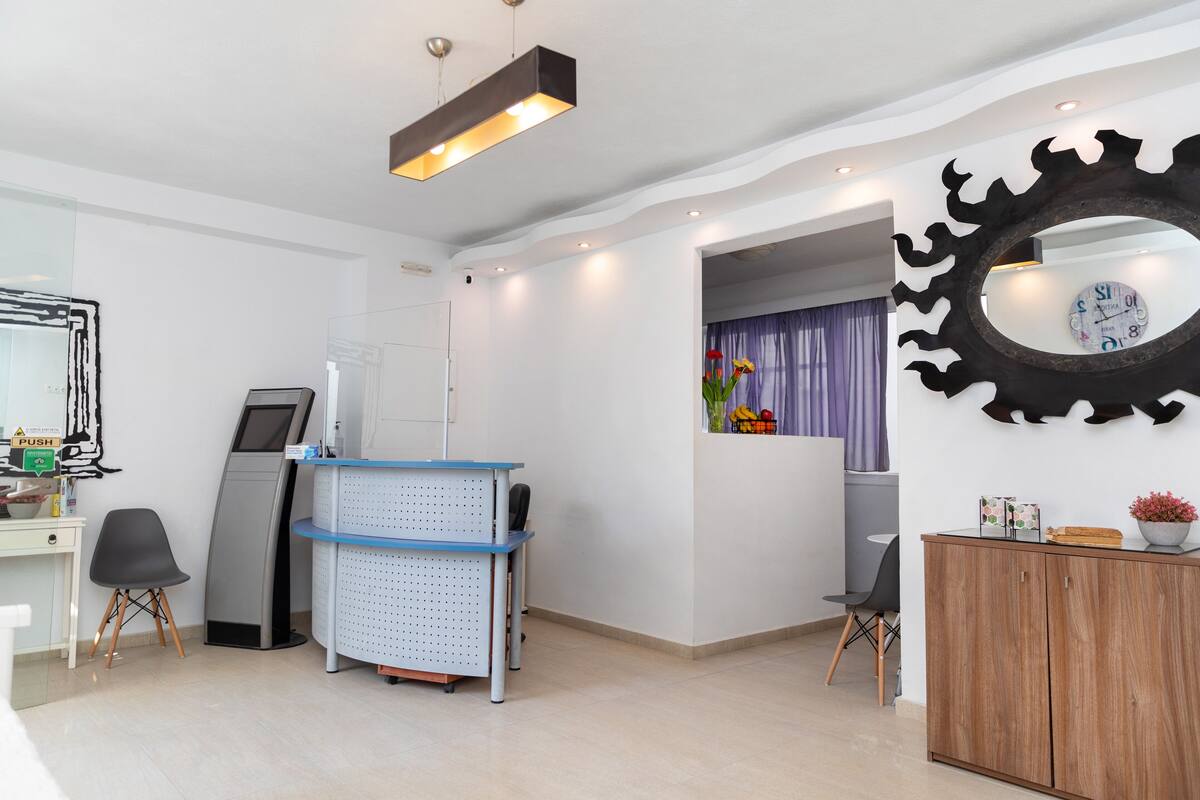 A reception area with a desk, chairs, a digital kiosk, and a decorative mirror.