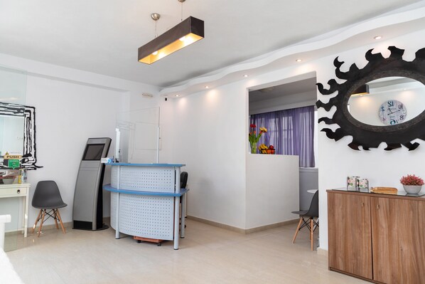 A reception area with a desk, chairs, a digital kiosk, and a decorative mirror.