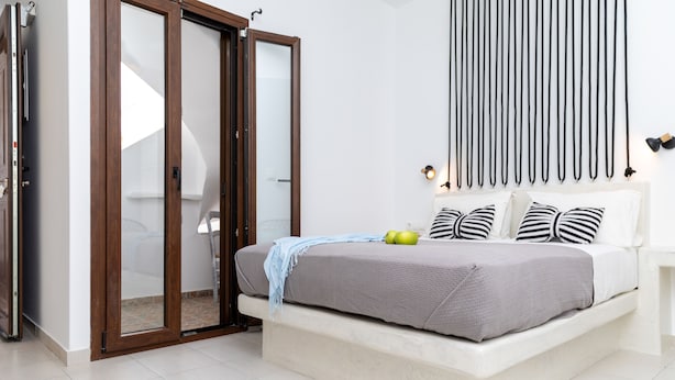 A bedroom with a bed, a sliding door, a wall-mounted light fixture, and a bedspread. - Depis Place & Apartments (Naxos)