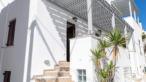 A white building with a staircase leading to a door, a palm tree in the foreground, and a clear blue sky. - Depis Place & Apartments (Naxos)