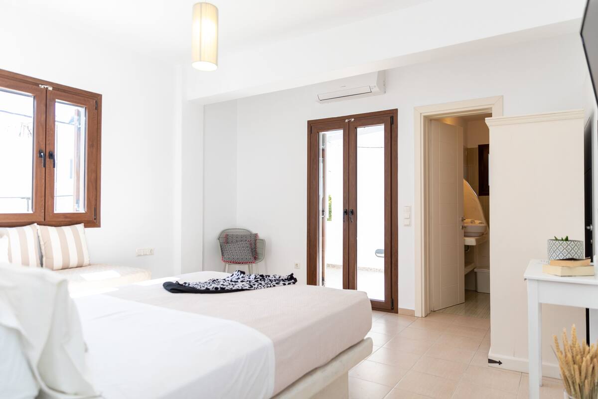A bedroom with a bed, a chair, a desk, and a door leading to a bathroom.