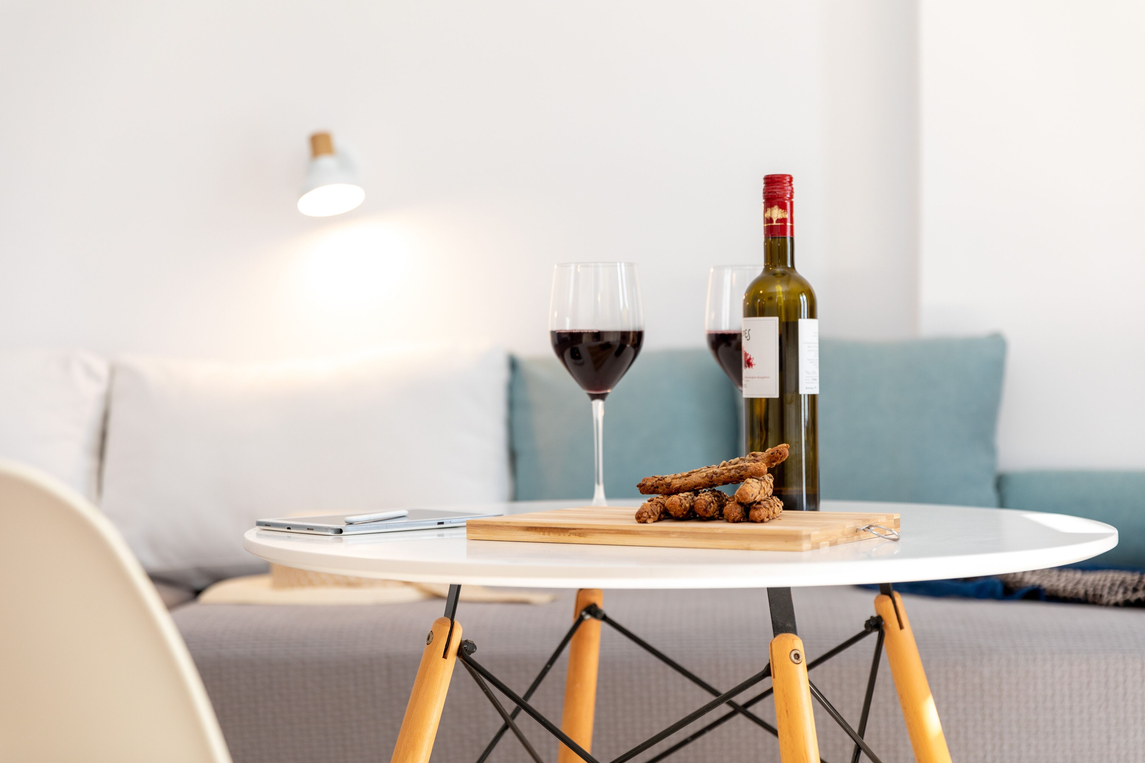 Una mesa redonda con una botella de vino, dos copas de vino tinto y una tabla de madera con rodajas de jengibre.