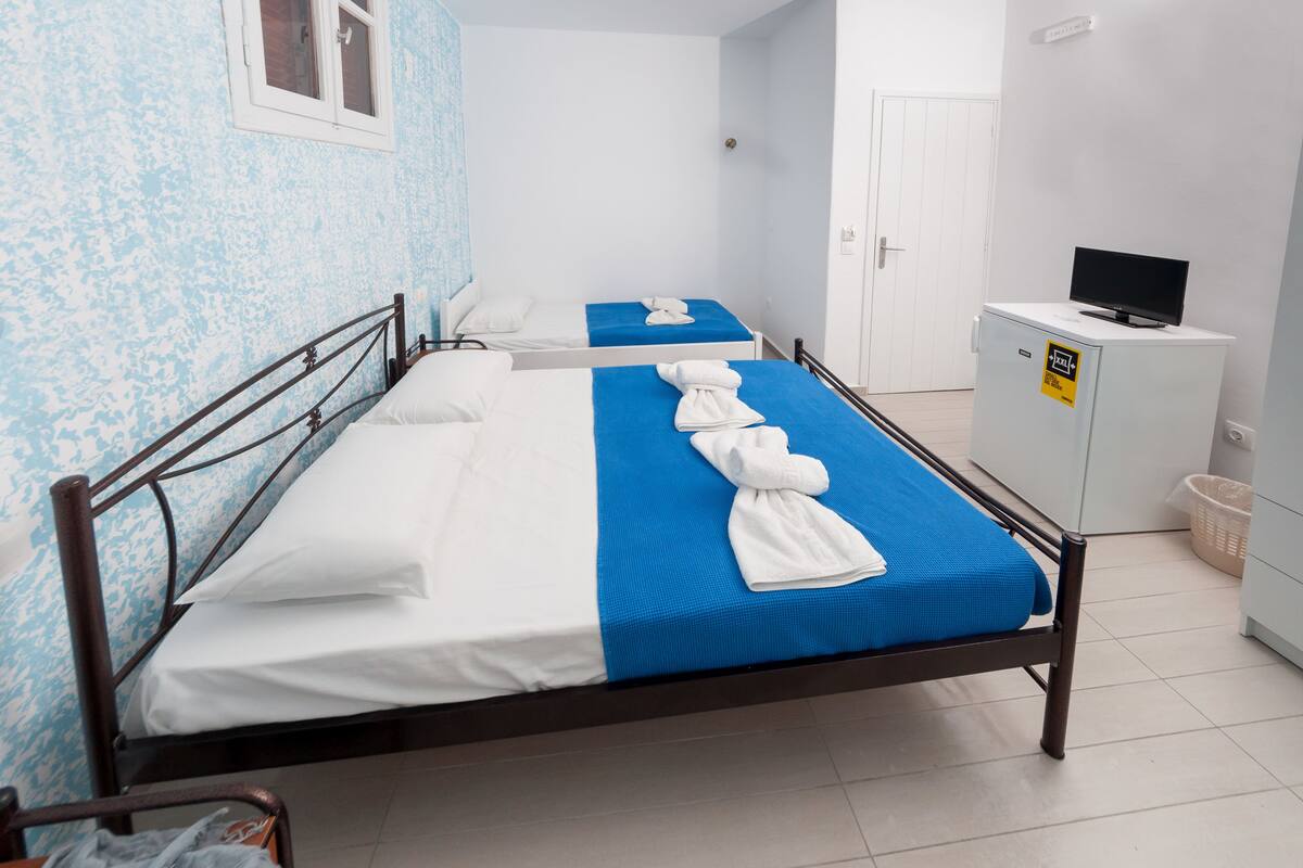 A room with two beds, each with a blue bedspread and white linens, and a white cabinet with a television on top.