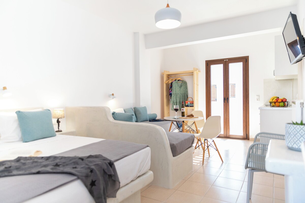 A modern hotel room with a bed, a sofa, a dining table, and a TV.