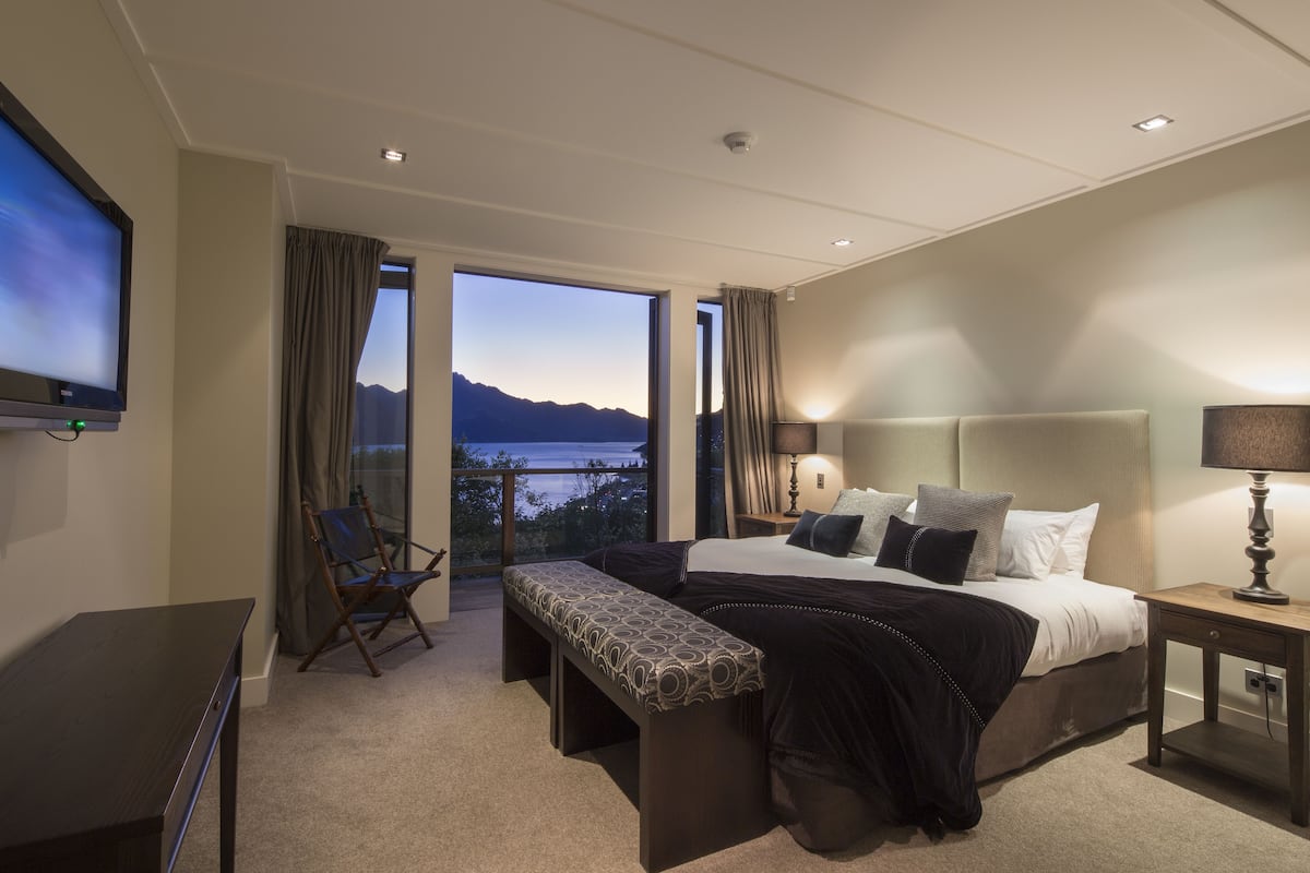Una habitación de hotel moderna con una cama grande, un escritorio, un banco y un televisor.
