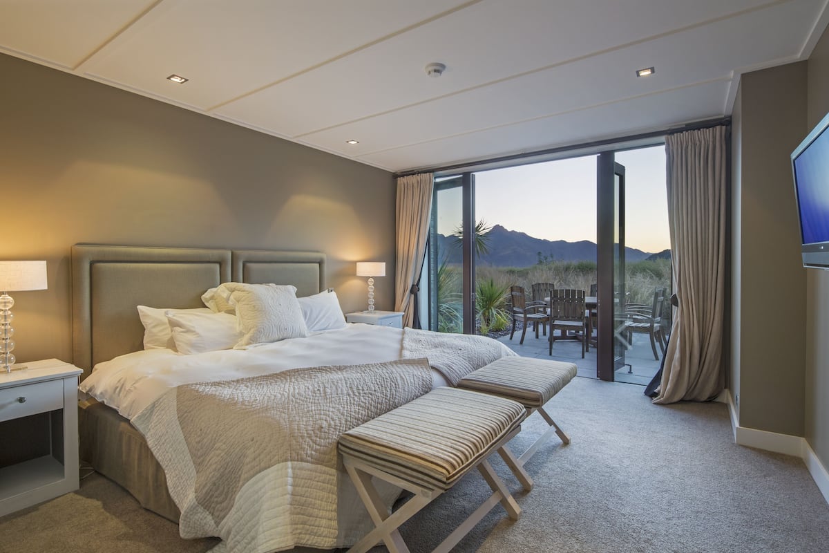 Habitación de hotel con una cama grande, un escritorio, una silla, un televisor y un balcón con vista a la montaña.