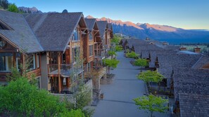 A row of wooden buildings with balconies, a paved pathway, and a mountain backdrop.