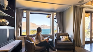 Ein Wohnzimmer mit Blick auf Berge und einen See, ausgestattet mit zwei Ledersofas und einem Glastisch.