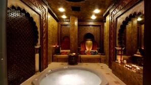 A traditional bath with a large, oval-shaped hot tub, ornate wooden walls, and a decorative alcove with candles. - Hotel Karolina (Sunny Beach)