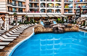 A swimming pool with lounge chairs and a water slide, surrounded by a multi-story hotel building with balconies. - Hotel Karolina (Sunny Beach)