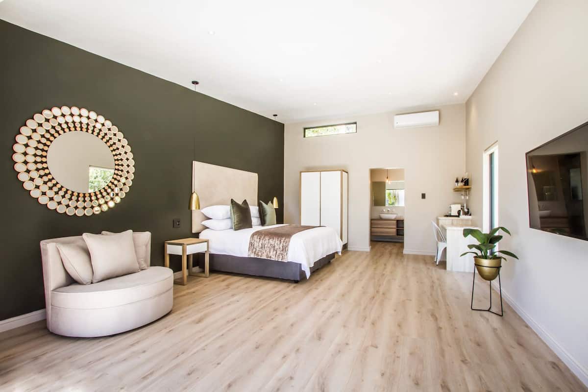 A modern bedroom with a large bed, a round mirror, a seating area, and a view of the bathroom.