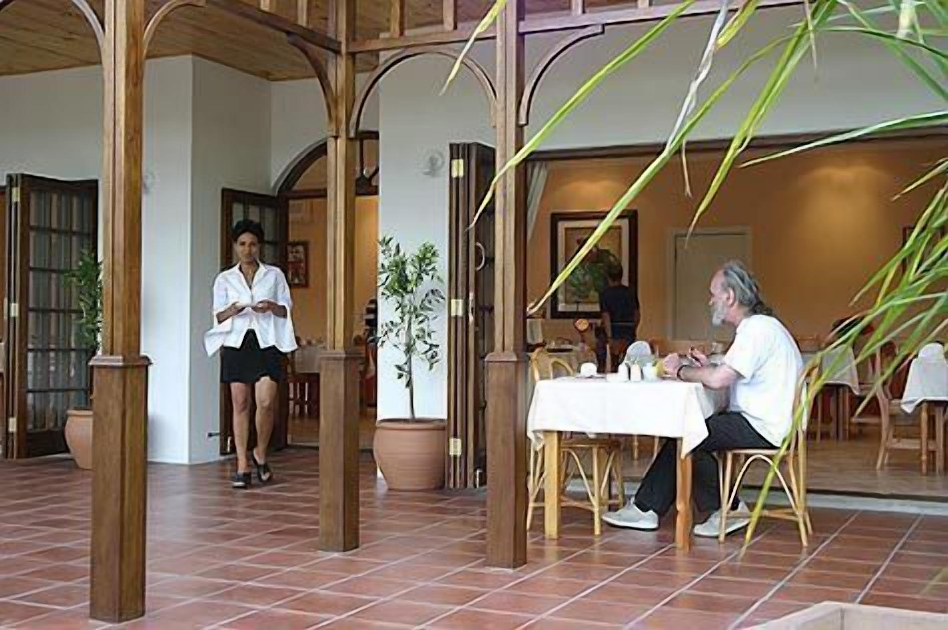 Una estructura de pérgola de madera con suelo de baldosas, una mesa con sillas y una planta en maceta.