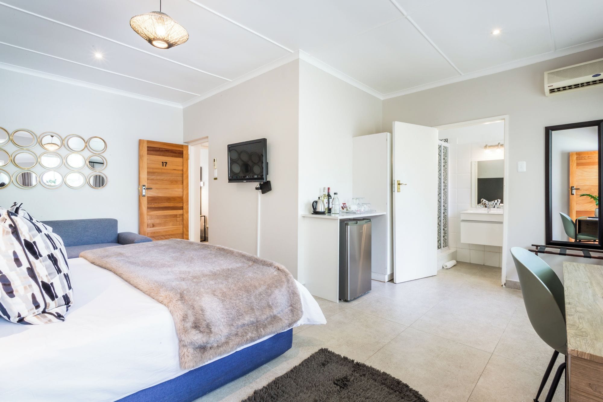 A modern bedroom with a bed, a desk, and a bathroom visible through an open door.