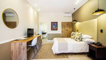 Una habitación de hotel moderna con un escritorio de madera, una cama con ropa blanca, un espejo redondo y un cuadro en la pared.
