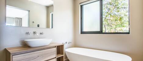 A modern bathroom with a freestanding bathtub, a large mirror, and a window providing natural light.