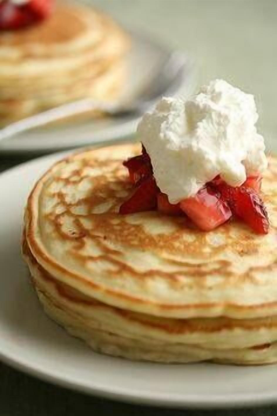 A stack of pancakes with a dollop of cream and sliced strawberries on top.
