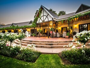 A hotel with a covered outdoor seating area, steps leading to the entrance, and lush greenery. - Hlangana Lodge (Oudtshoorn)