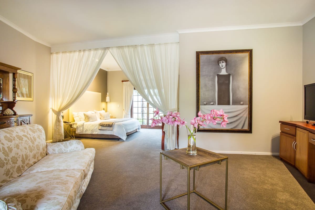 A hotel room with a bed, a sofa, a small table with a vase of flowers, a painting on the wall, and a television on a wooden cabinet.