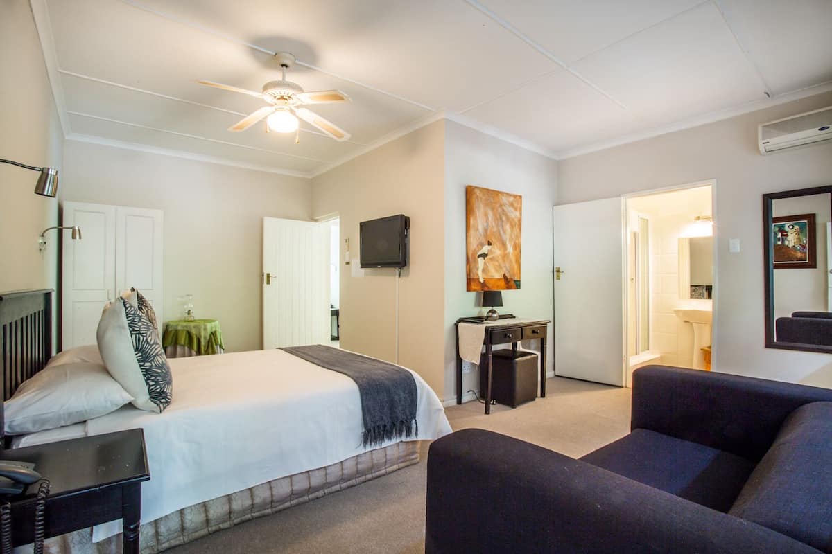 A hotel room with a bed, a desk, a chair, a ceiling fan, and a TV.