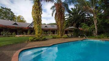 A swimming pool surrounded by palm trees and a building with a sloped roof.