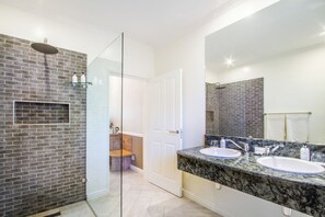 A modern bathroom with a glass shower enclosure, two sinks with granite countertops, and a large mirror. - Hlangana Lodge (Oudtshoorn)