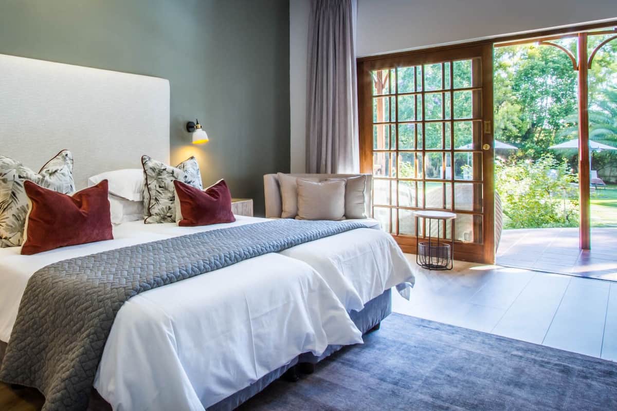 A modern bedroom with a large bed, two bedside tables, and a view of a garden through a glass door.