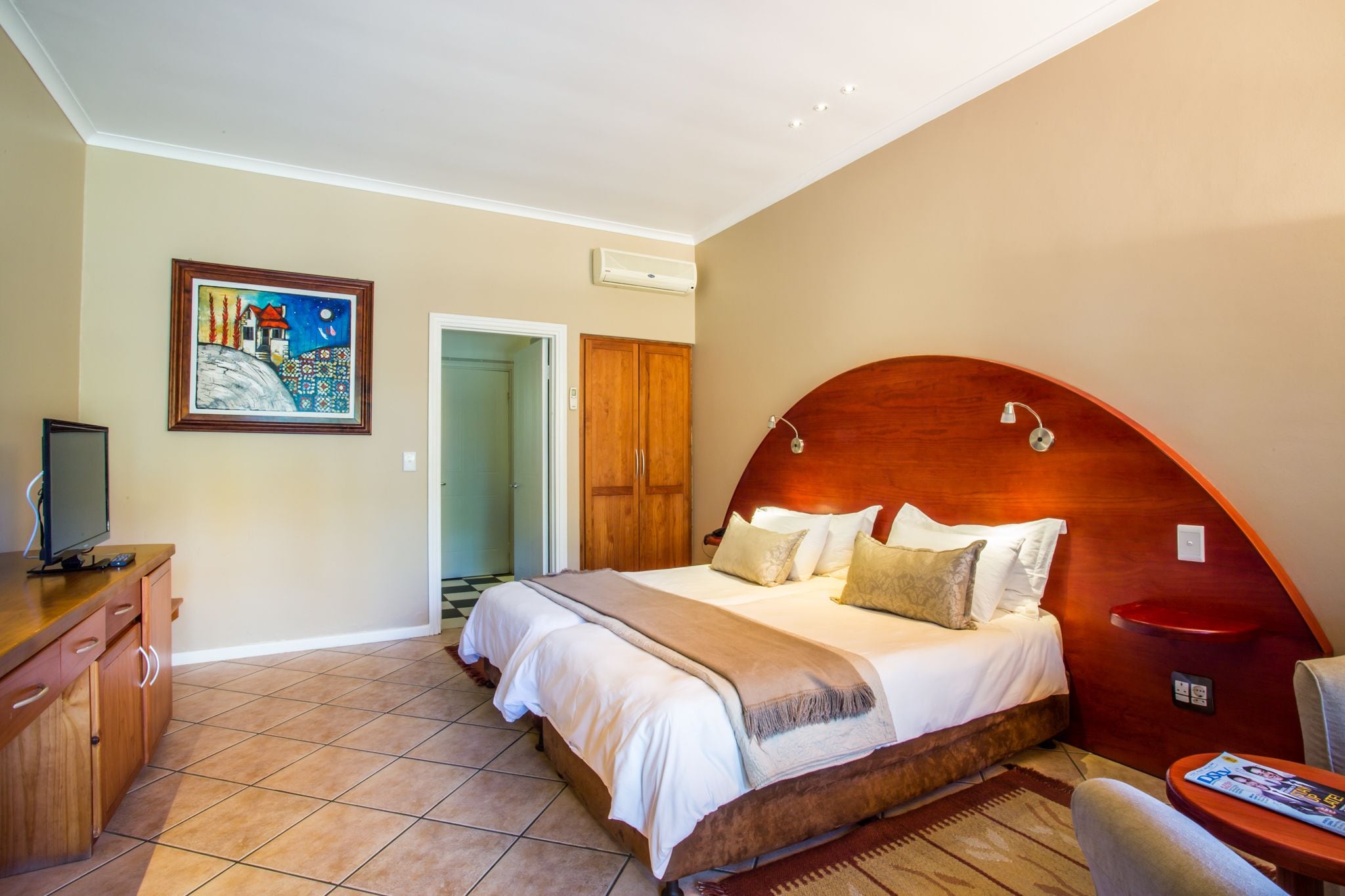 A bedroom with a large bed, a wooden headboard, a television on a wooden dresser, and a painting on the wall.