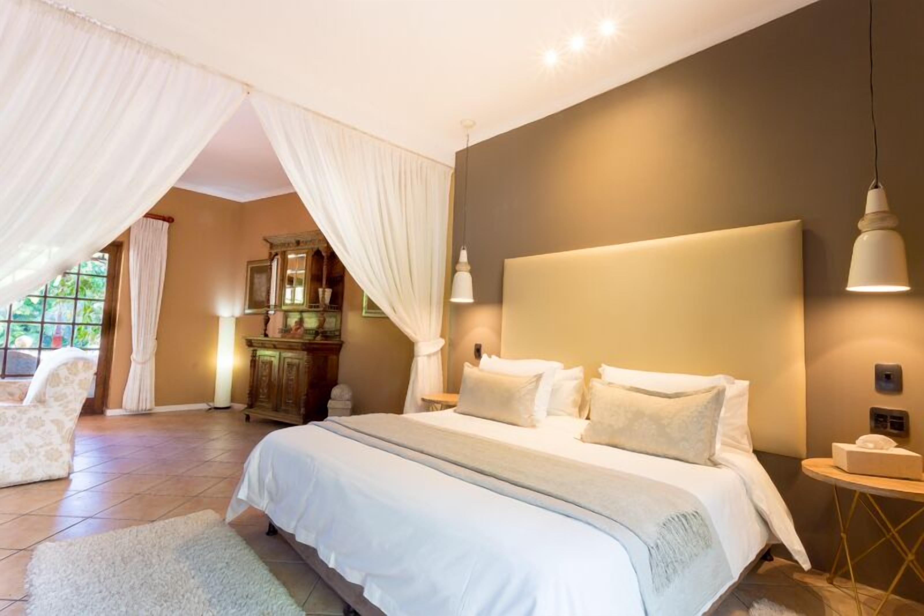 A bedroom with a large bed, a nightstand, a lamp, and a window with curtains.