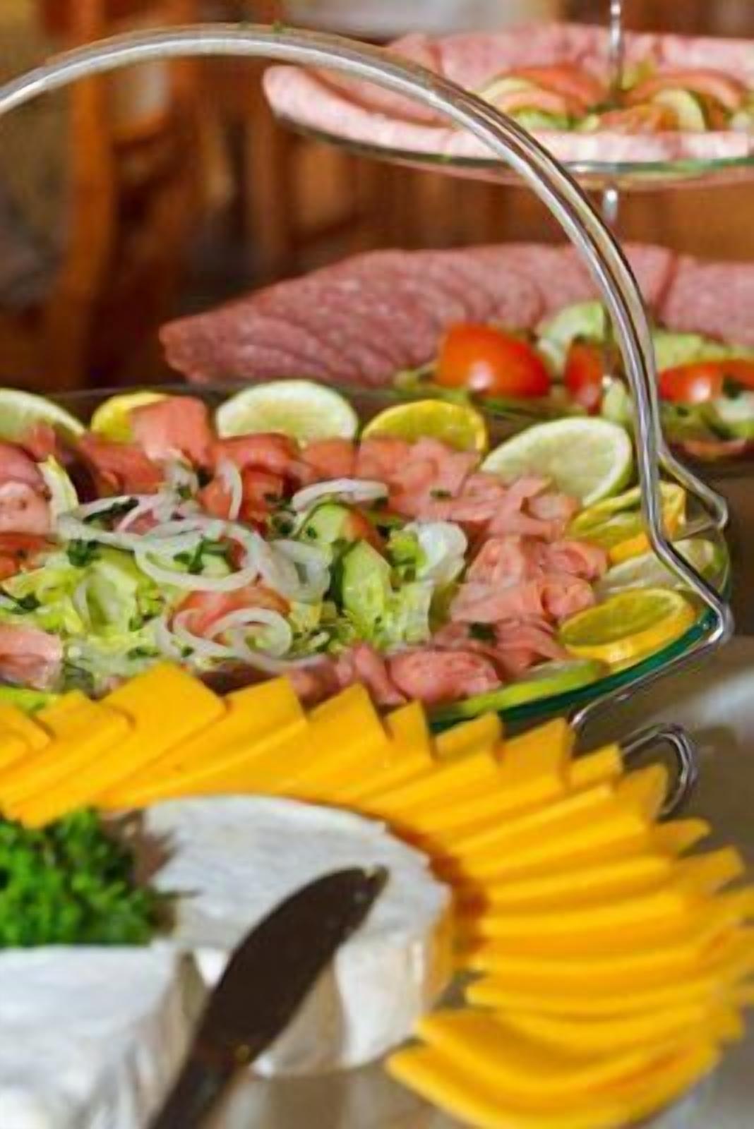Un bufé con diversas opciones de comida, incluyendo carnes cortadas, verduras y queso.