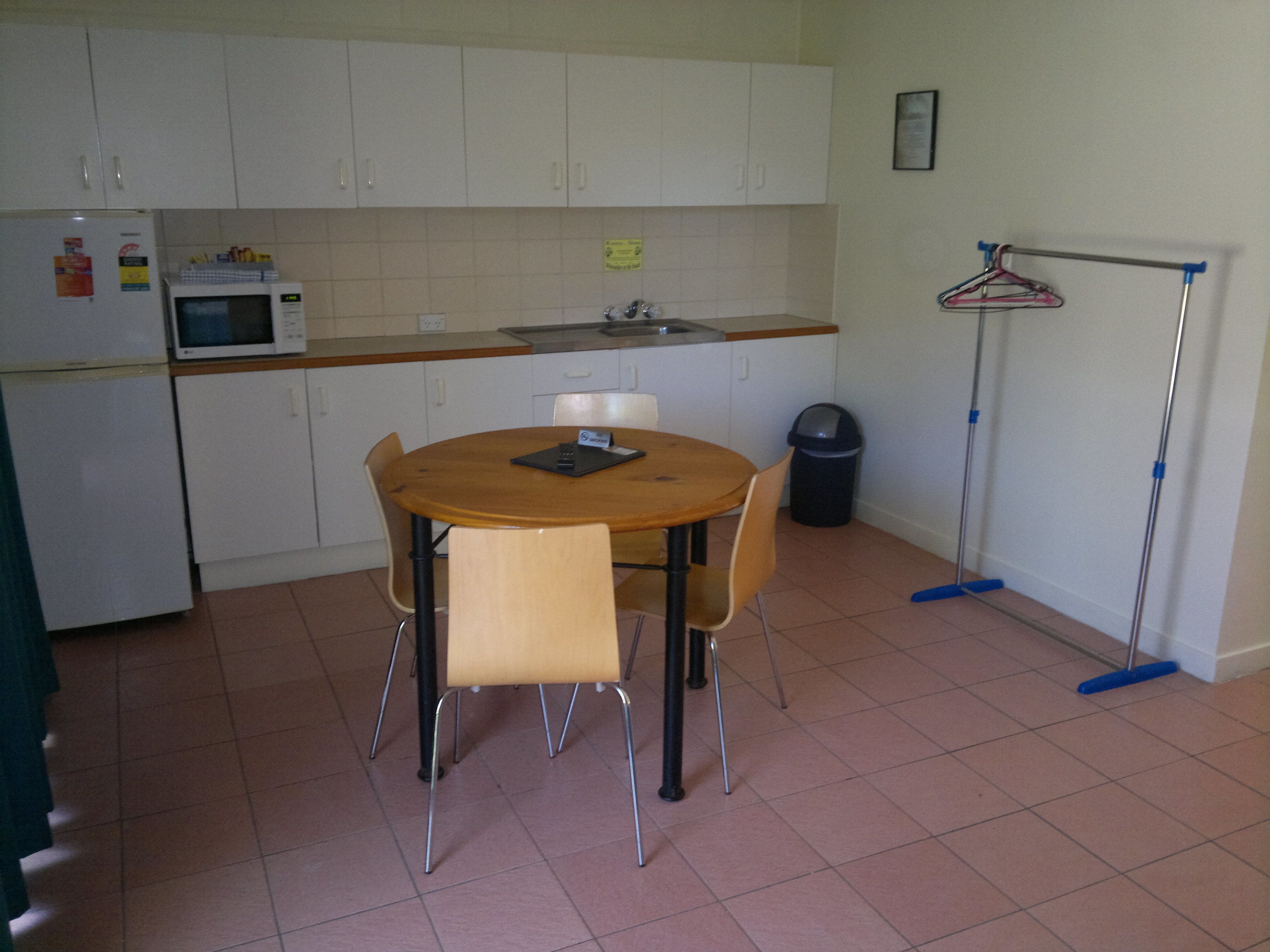 A small kitchen with white cabinets, a microwave, a sink, and a round table with chairs.
