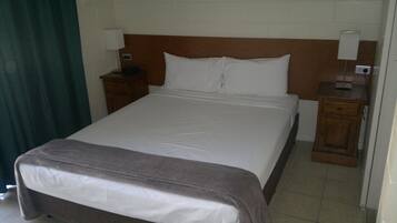 Een standaard hotelkamer met een enkel bed, houten hoofdbord, twee nachtkastjes met lampen en een groen gordijn.