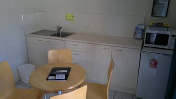 A small kitchenette with a sink, microwave, and refrigerator. There is a table with two chairs and a sign prohibiting smoking.