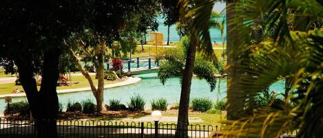 Zona de piscina con un puente, rodeada de árboles y una valla.