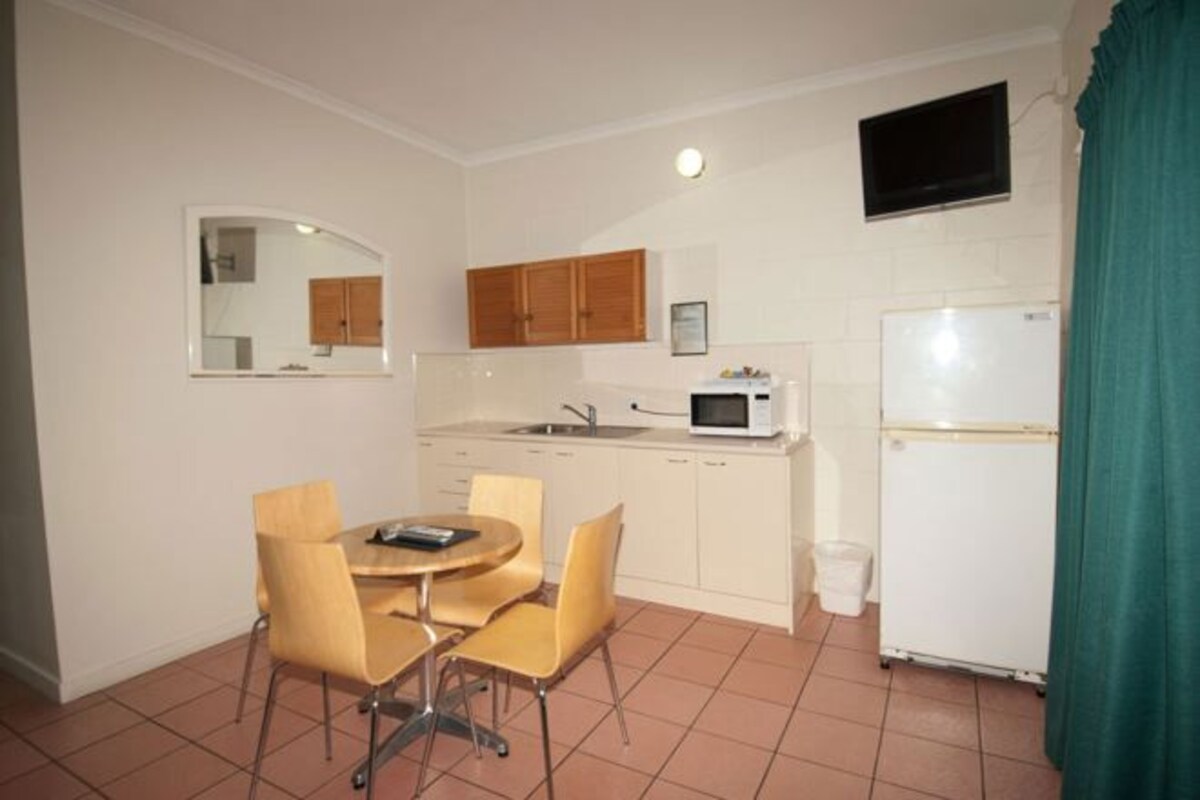 A compact kitchen with a dining table and chairs, a microwave, a refrigerator, and wooden cabinets.