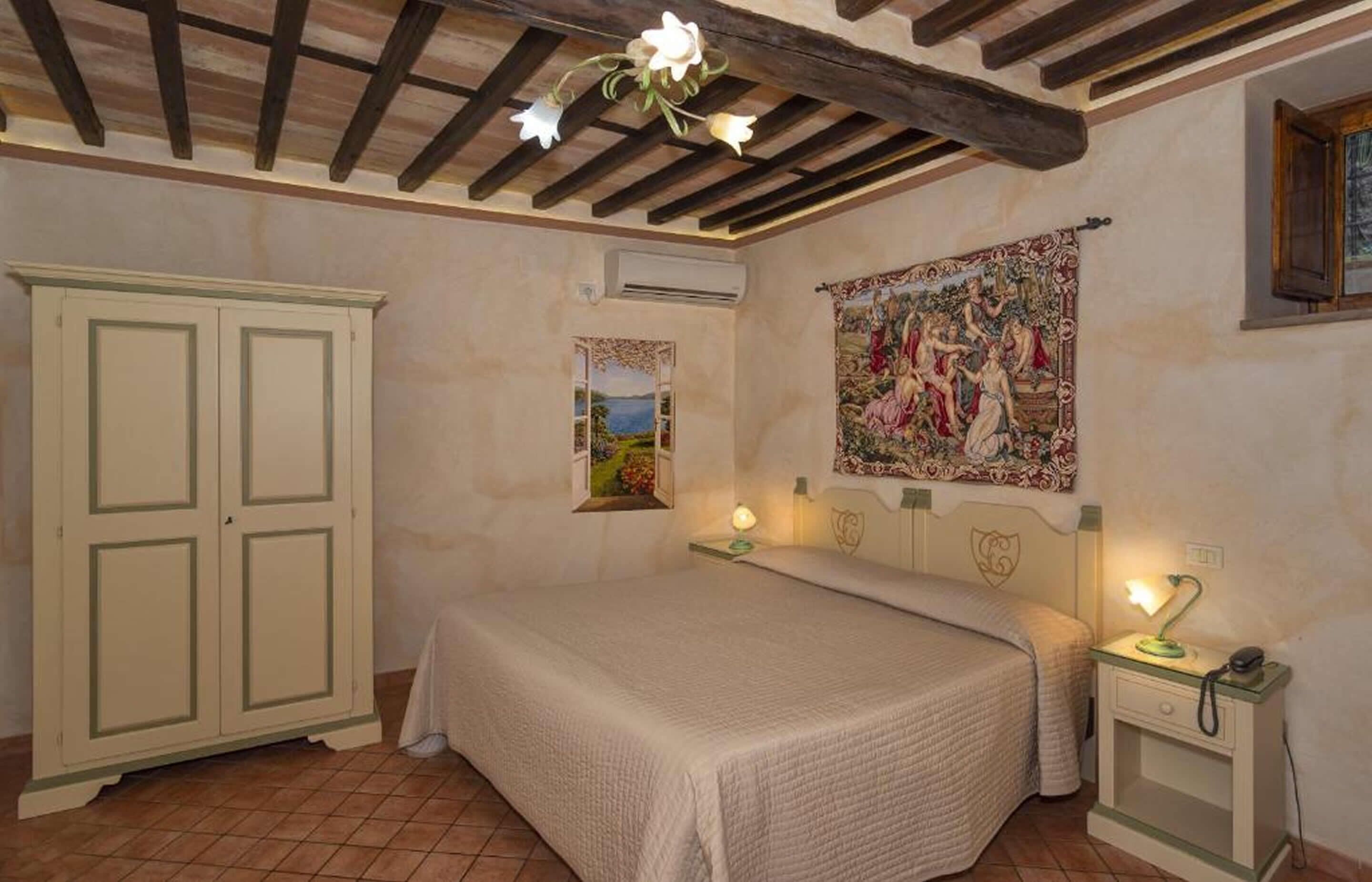Una camera da letto con un letto, abat-jour, comodino, armadio, arazzo e finestra con vista.